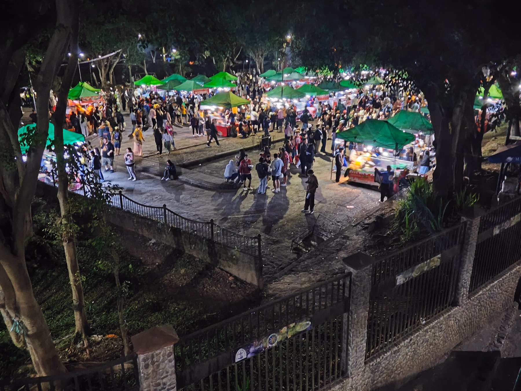 Food stalls with green tents and visitors in the Baguio night market area