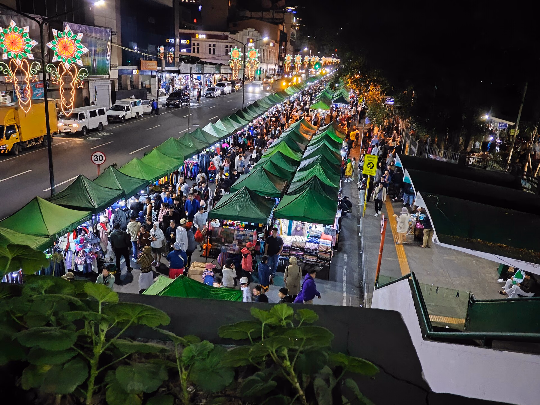 Rows of green market tents and dense crowds along Harrison Road at night